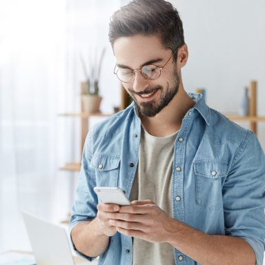 Ein Mann schaut auf ein Smartphone. Er lächelt und wirkt zufrieden.